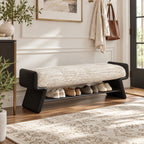 Bench with a cream upholstered cushion, black shaped side panels and a lower shelf holding shoes.