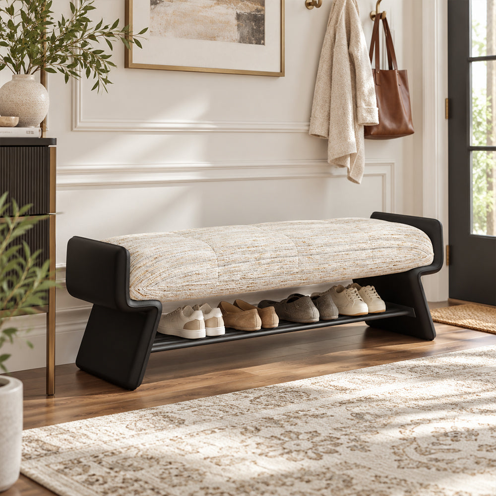 Bench with a cream upholstered cushion, black shaped side panels and a lower shelf holding shoes.