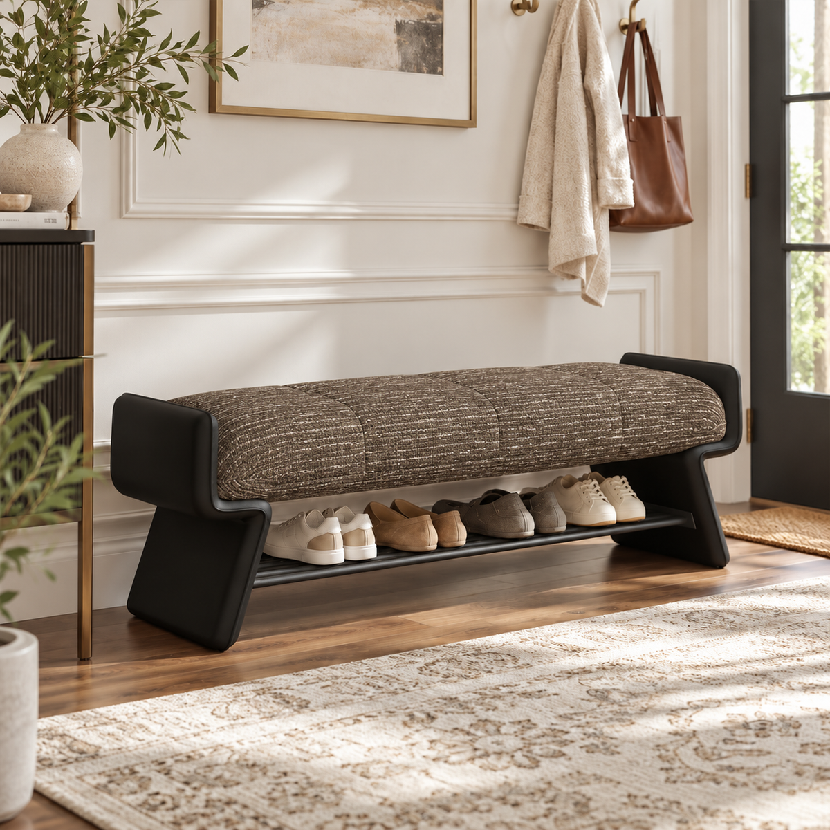 Bench with a dark taupe upholstered cushion, black shaped side panels and a lower shelf holding shoes.