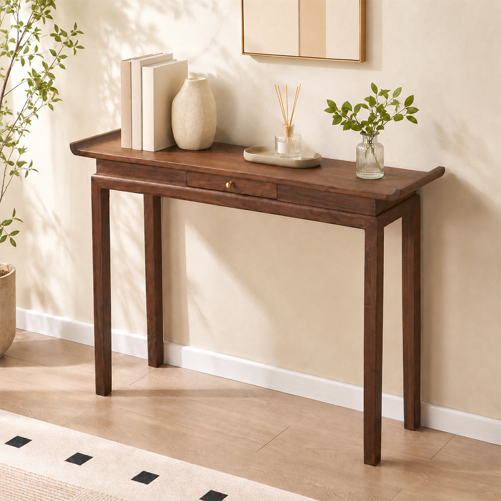 Brown drawer console table styled with vases and books against a pale entryway wall.